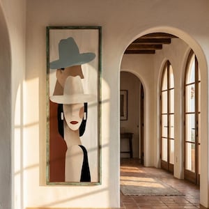 Puede incluir: Una pieza de arte mural enmarcada de forma rectangular vertical que presenta una ilustración estilizada de dos figuras con sombreros. La figura superior lleva un sombrero azul claro y la inferior uno blanco, con tonos marrones, negros y crema.