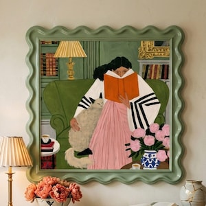May include: A framed wall art print featuring a person reading an orange book while sitting on a green sofa with a cat. The illustration includes a lamp, a vase of pink flowers, and bookshelves. The frame has a wavy, sage green border design.