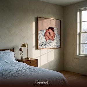 japandi wall art in a sunlit bedroom. A slim wood frame holds a warm terracotta figure painting on a plaster wall, with a brass lamp, a wood nightstand and a dried rose lit by soft natural window light.