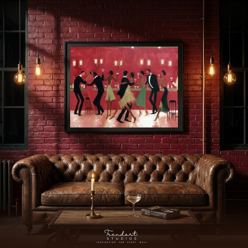 May include: A framed artwork showing a jazz club scene with people dancing and drinking. The painting hangs above a brown leather sofa, with a candle, a glass of wine, and a book on a wooden coffee table. The wall is red brick.