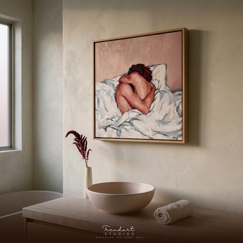 wabi sabi wall art in a neutral plaster room. A light oak floating frame surrounds a soft terracotta figure painting above a wood console with a rounded stone vessel bowl and a single dried branch.