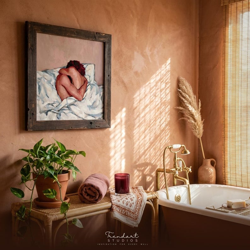 terracotta wall art for a boho bathroom. A rustic reclaimed wood frame holds a warm figure oil painting above a freestanding tub, pampas grass, a trailing pothos plant and a softly glowing candle.