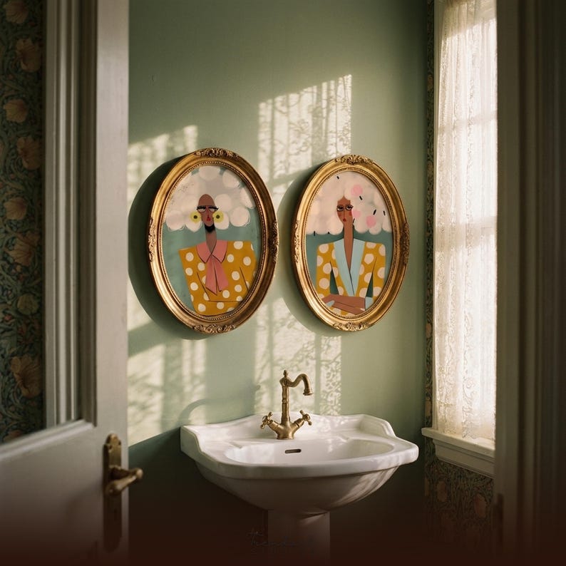 Funny bathroom wall art — two women prints in ornate gold oval frames above white pedestal sink, sage green powder room walls, natural window light with lace curtain