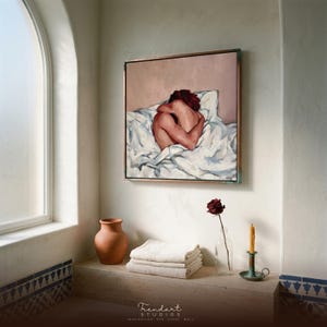 mediterranean bathroom wall art in a white arched alcove. A framed figurative painting in warm terracotta tones hangs above a niche with stacked towels, a clay vase, a single dried rose and blue patterned tiles.