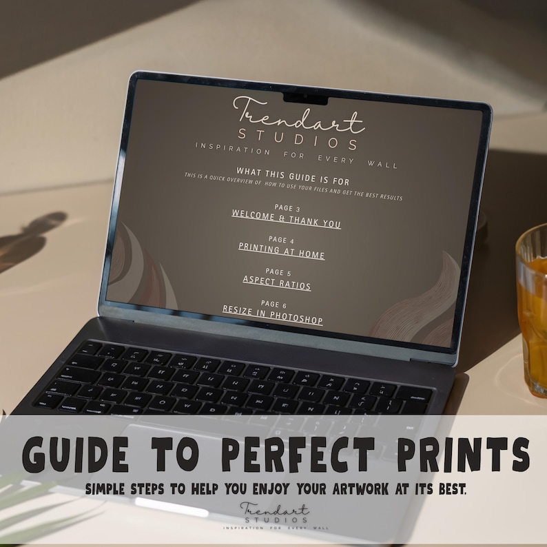 Laptop screen displaying a digital guide to perfect prints manual next to a glass of juice on a desk