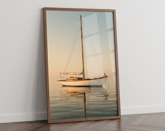 May include: A framed print of a sailboat on calm water. The boat is white with a wooden deck and mast, reflecting in the water. The sky transitions from a soft orange to blue, creating a serene nautical scene.