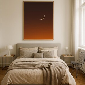 May include: A bedroom scene featuring a large framed print of a crescent moon against a gradient orange and brown sky. The bed is made with beige linens and a brown throw blanket. Two bedside tables with lamps flank the bed. A black wire chair sits near a window.