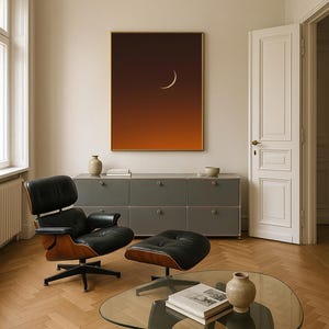 May include: Interior shot featuring a modern living room with a black leather chair and ottoman. A glass coffee table holds a book and vase. A framed art piece with a crescent moon hangs above a gray cabinet. The room has hardwood floors.