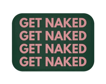 Pode incluir: Um tapete de banho retangular com cantos arredondados. O tapete é verde escuro com a frase "GET NAKED" repetida quatro vezes em rosa, numa fonte sem serifa. O texto está centrado e uniformemente espaçado.