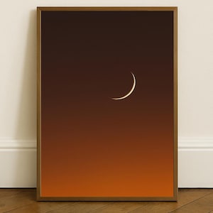 Pode incluir: Uma impressão artística emoldurada com uma lua crescente contra um fundo gradiente de tons laranja e castanho. A obra de arte é apresentada numa moldura de madeira, criando uma estética minimalista. Um item de decoração para casa com tema celestial.