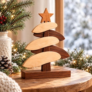 Peut inclure: Un sapin de Noël décoratif en bois composé de branches horizontales alternant bois clair et bois foncé fixées sur un mât central, surmonté d'une étoile à cinq branches et posé sur un socle rectangulaire en bois foncé.