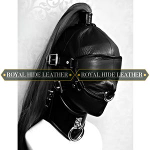 Pode incluir: Capuz de couro preto com rabo de cavalo alto, anéis de metal e fivelas. O capuz cobre a cabeça e o rosto, com uma venda e uma abertura para a boca. O texto "ROYAL HIDE LEATHER" é exibido na imagem.