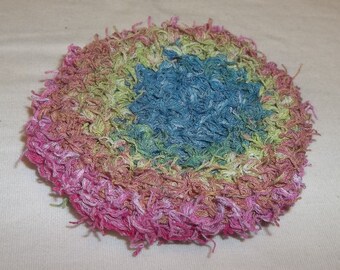 May include: A round, crocheted potholder with a multi-colored design. The potholder is pink, green, blue, and white. It has a fringed edge.