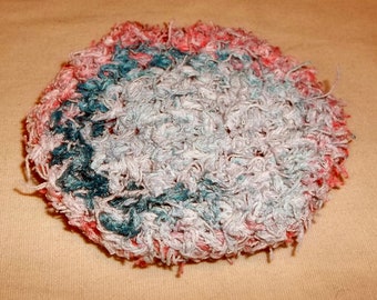 May include: A round, crocheted scrubby with a pink, white, and blue color scheme. The scrubby is made of soft, fluffy yarn and has a textured surface.