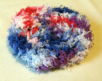May include: A round, fluffy, crocheted potholder in shades of pink, blue, white, and purple.