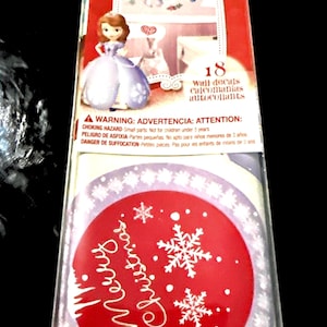 May include: A package of Disney wall decals featuring a princess and other decorative elements. The package includes a red circle with the words "Merry Christmas" and snowflakes. The package also includes a warning about choking hazards.