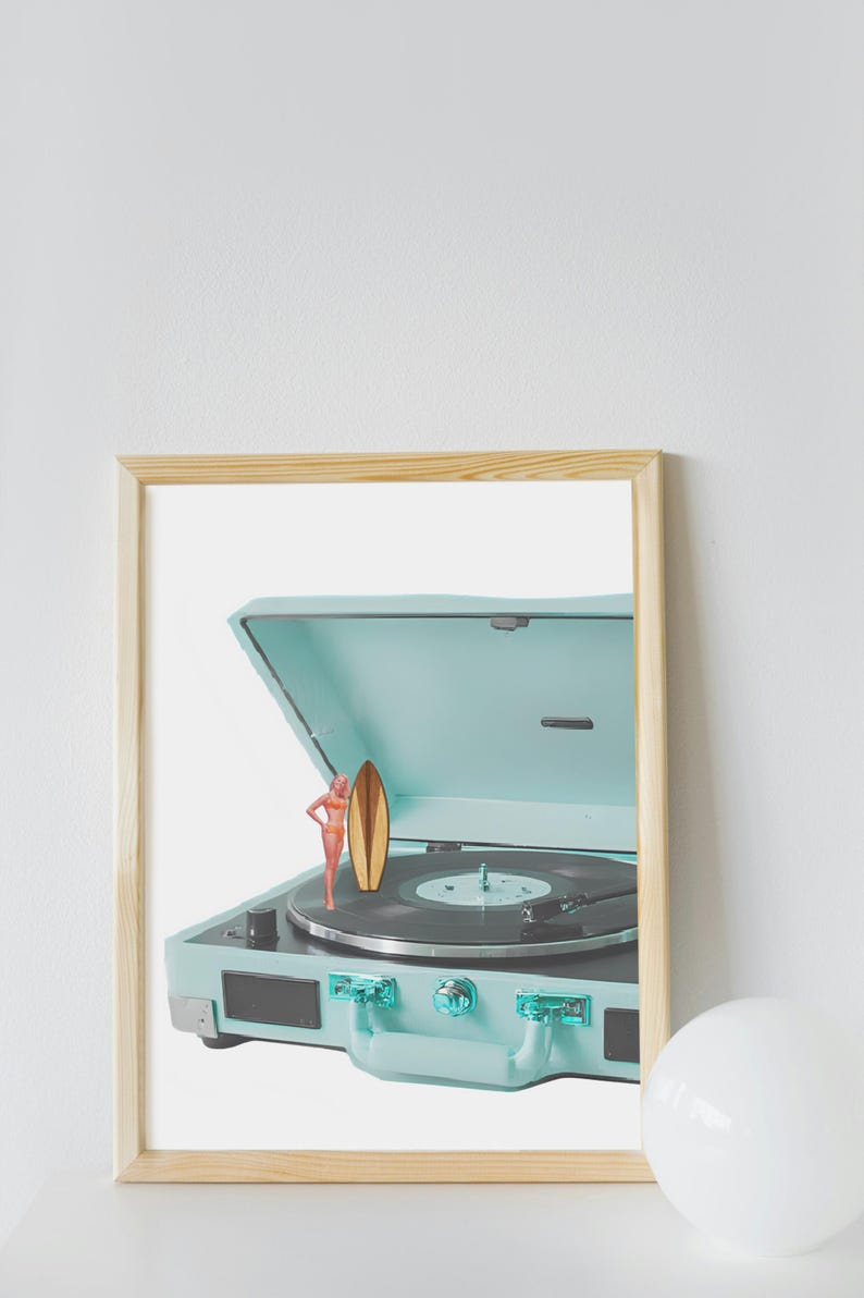 May include: A framed print featuring a vintage-style, light blue record player with a miniature surfboard and a figurine of a person in a swimsuit. The record player is open, revealing a black vinyl record.