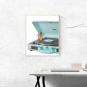 May include: A framed image of a vintage-style, light blue record player with a vinyl record on the turntable. A small figurine of a person holding a surfboard is on top of the record player. The record player is open, revealing the turntable.