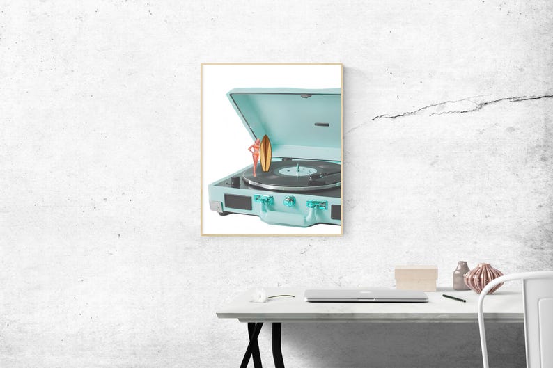 May include: A framed image of a vintage-style, light blue record player with a vinyl record on the turntable. A small figurine of a person holding a surfboard is on top of the record player. The record player is open, revealing the turntable.