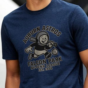Op de afbeelding: Marineblauw t-shirt met de tekst "AUBURN ASTROS" en een cartoon honkbalspeler. Het shirt bevat ook "FALCON PARK NY-PENN LEAGUE EST. 1958". Het shirt is gemaakt van een zacht materiaal.