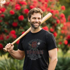May include: Black t-shirt featuring the Lancaster Red Roses baseball team logo. The design includes a rose character holding a bat and baseball. The text reads "Lancaster, PA Tri-State League Stumpf Field Est. 1906". A wooden baseball bat rests on the shoulder.