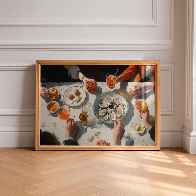 May include: A framed print of a dining scene with a table set for a meal. The table is covered with a floral tablecloth and features plates of food, drinks, and a platter of oysters. People are gathered around the table.