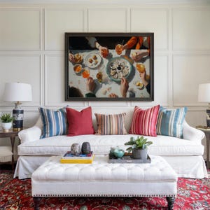 May include: A living room scene featuring a white sofa adorned with colorful throw pillows. Above the sofa hangs a framed painting depicting a dining scene. A tufted ottoman and a patterned rug complete the cozy, inviting space. Two lamps flank the sofa.