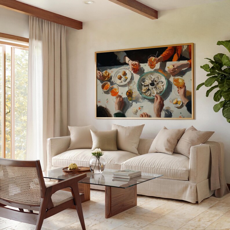 May include: A framed painting depicts a dining scene with a table set with oysters, drinks, and small plates. The painting hangs above a beige sofa with throw pillows. A glass coffee table and wooden chair are in front of the sofa.