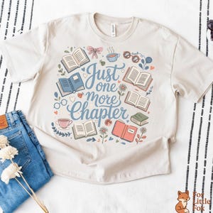 以下が含まれることがあります： クリーム色のTシャツ。開いた本、花、ティーカップ、メガネの気まぐれなデザインが特徴です。「Just one more chapter」というフレーズがソフトブルーのスクリプトで書かれています。このシャツはブルージーンズと組み合わせています。