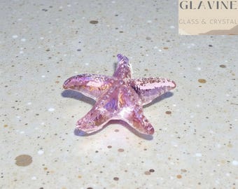 May include: A translucent, light pink glass starfish figurine with an iridescent, shimmering finish. The five-pointed object features a textured, bumpy surface that catches the light, creating subtle reflections across its crystalline structure.