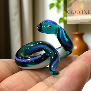 May include: A glass snake figurine in teal, blue, and black. The snake is coiled, with a white underside. This decorative item could be a paperweight or a collectible ornament.