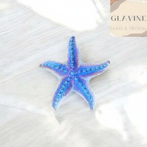 May include: A five-pointed starfish figurine featuring a vibrant blue and purple iridescent finish with a textured, bumpy surface. The object displays a glossy sheen and is positioned centrally, showcasing its distinct radial symmetry and detailed arms.