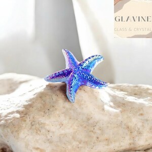 May include: A vibrant blue and purple iridescent glass starfish figurine with a textured surface. The object features a glossy finish that reflects light, showcasing a gradient of deep blue to violet hues across its five pointed arms.