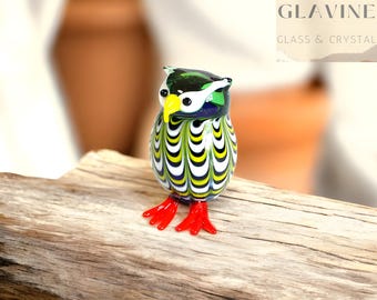May include: A colorful glass owl figurine with a green, yellow, and white patterned body, a yellow beak, and red feet. The owl is perched on a piece of driftwood. The owl is approximately 3 inches tall.