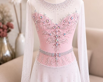 May include: A long-sleeved ice skating dress featuring a pale pink bodice and a white skirt. The garment is adorned with intricate silver beadwork, clear crystals, and iridescent marquise-shaped stones arranged in a symmetrical floral pattern.