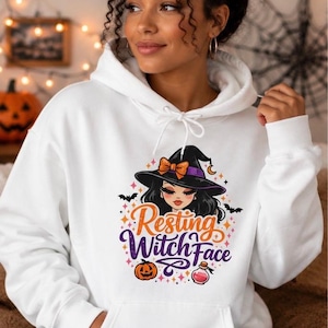 May include: A white hooded sweatshirt featuring a graphic print of a witch wearing a black hat with an orange bow. The text Resting Witch Face is printed in orange and purple, accompanied by illustrations of a pumpkin, a potion bottle, and bats.