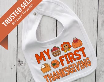 Puede incluir: Babero blanco para bebé con el texto "MY FIRST THANKSGIVING" en naranja. El babero presenta ilustraciones de una tarta de calabaza, una calabaza, una cesta de manzanas, un pavo y una calabaza con un lazo.