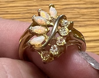 May include: A gold-toned ring featuring a cluster of oval-shaped opals and small, round clear gemstones. The ring has a leaf-like design with a curved band. The opals have a milky, iridescent appearance.