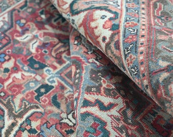 Op de afbeelding: Close-up van een opgerolde, antieke tapijt met een gedetailleerd, vervaagd patroon. Het tapijt heeft een complex ontwerp in tinten rood, blauw en beige. Het ingewikkelde patroon is zichtbaar en toont de leeftijd en het vakmanschap van het tapijt.