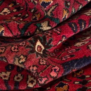 May include: Close-up of a richly patterned rug with a deep red background. The rug features intricate floral and geometric designs in shades of blue, green, beige, and brown. The texture appears soft and plush.