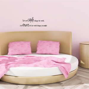 May include: A pink round bed with two pink pillows and a pink blanket. The wall behind the bed is light pink and has a black quote on it that reads "Let your smile change the world, but never let the world change your smile."