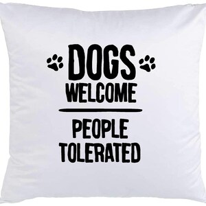 May include: White pillow with black text that reads "Dogs Welcome People Tolerated" with paw prints on either side of the word "Dogs".