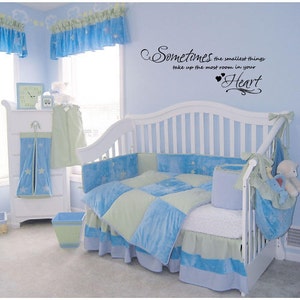 May include: A white crib with a blue and green bedding set. The crib has a quote on the wall above it that reads "Sometimes the smallest things take up the most room in your Heart".