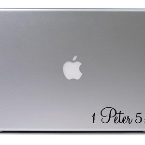 May include: A silver laptop with a white Apple logo on the top. The text "1 Peter 5:7" is written in a cursive font on the lower right corner of the laptop.