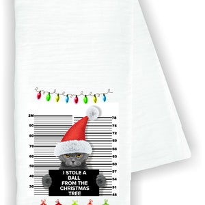 May include: A gray cat wearing a Santa hat holds a sign that reads "I stole a ball from the Christmas tree". The cat is standing in front of a white background with a height chart and a string of Christmas lights.