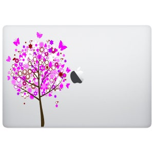 Könnte beinhalten: Ein Laptop mit einem Aufkleber mit einem rosa und weißen Blumenbaumdesign auf der Rückseite. Der Baum hat Schmetterlinge und Blumen in den Farben Rosa, Weiß und Rot.