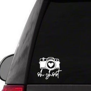 May include: White vinyl decal with a camera silhouette and a heart in the lens. The text "oh shoot" is written below the camera.