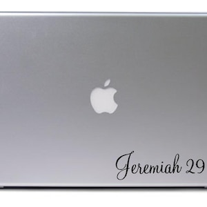 May include: A silver laptop with a white Apple logo and a black vinyl sticker with the text "Jeremiah 29:11".