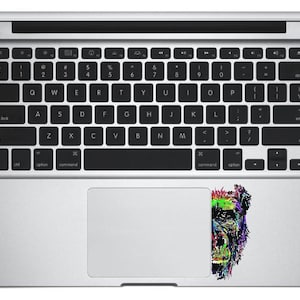 May include: A silver laptop computer with a colorful sticker of a monkey's face on the trackpad.