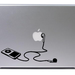 Può includere: Un computer portatile argentato con un adesivo in bianco e nero di un iPod, cuffie e un logo Apple.